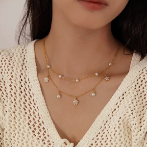 Close-up of double-layer gold necklace with white pearl accents and floral pendant