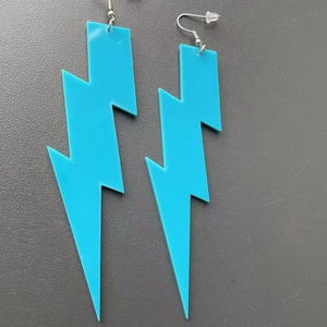 Close-up of vibrant blue acrylic lightning bolt earrings with secure silicone backs