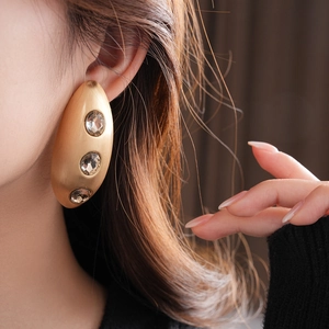 Close-up of model wearing large gold brushed metal earrings with inlaid crystals