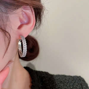 Close-up of silver hoop earring with sparkling zircon leaf patterns worn by a model