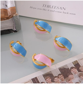 Detailed shot of retro C-shaped enamel earrings in gold, pink, and blue color blocking