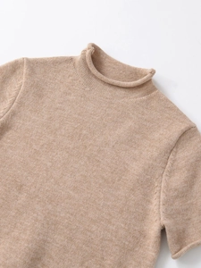 Detail of light camel knit top featuring a ribbed high neck and soft wool texture