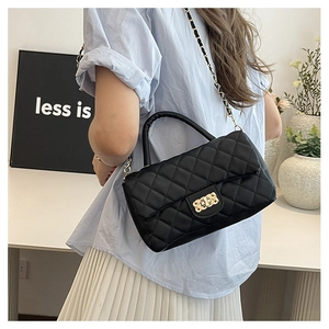 Detail of black quilted leather handbag with gold chain strap and twist lock on a table