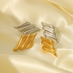 Minimalist 18k gold and silver wing-shaped stainless steel earrings on beige silk fabric