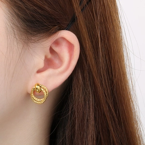 Detailed close-up of double-loop gold earrings with elegant twisted texture on ear