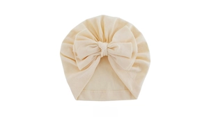 Detail of a soft beige baby turban hat featuring a large decorative bow on white background