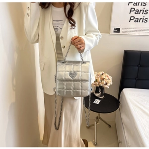 Detail of silver quilted backpack featuring a heart-shaped metal clasp and chain strap