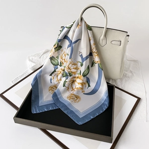 Detail of satin floral scarf with yellow flowers and blue borders on a wooden tray
