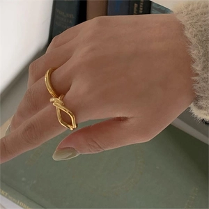 Close-up of a minimalist golden knotted ring worn on a finger with a vintage aesthetic