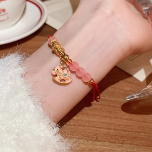 Détail du bracelet tressé rouge avec perles roses et breloque cheval à bascule doré