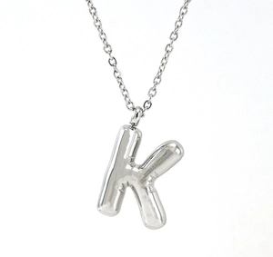 Macro detail of silver bubble letter K pendant in polished stainless steel