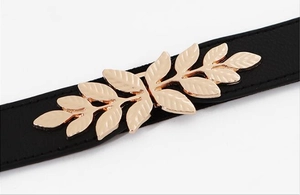 Detail shot of the golden leaf metal buckle on a black elastic waist belt