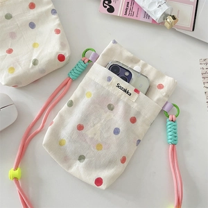 Detailed view of polka dot canvas phone pouch with pink strap and lifestyle items