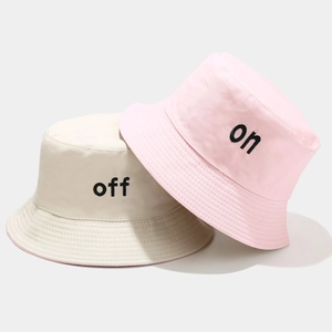 Détail de bobs en coton avec broderie noire 'on' et 'off' en couleurs beige et rose