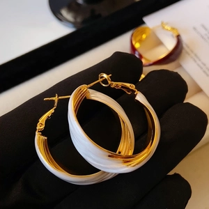 Vintage gold and white twisted U-shape hoop earrings held by a black gloved hand