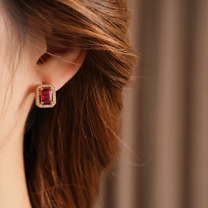 Close-up of elegant gold square earrings featuring a large red gemstone and zircon accents