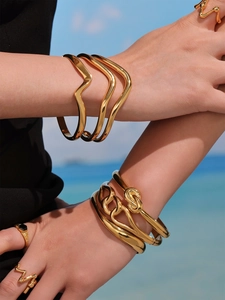 Macro detail of geometric twisted 18k gold plated bangle and wave ring on a model