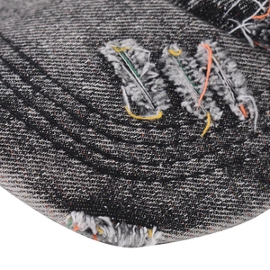 Detail of washed grey denim cap showing distressed holes and colorful contrast stitching