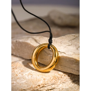 Macro shot of 18k gold plated hollow circular pendant on black wax cord over stone
