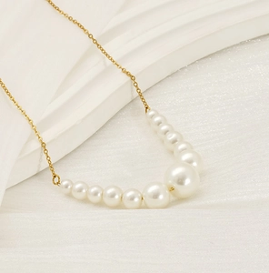 Detail of elegant gold chain necklace featuring gradient white pearls on silk background
