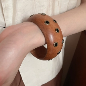 Gros plan d'un large bracelet en bois marron avec des rivets métalliques vintage au poignet