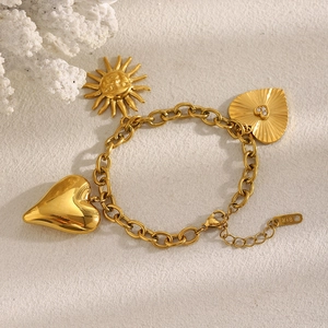 Detail of 18K gold-plated O-chain bracelet with sun and heart charms on a sandy backdrop