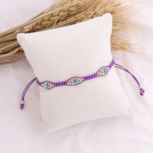 Detail of a purple woven bohemian bead bracelet on a white cushion with dried wheat decoration