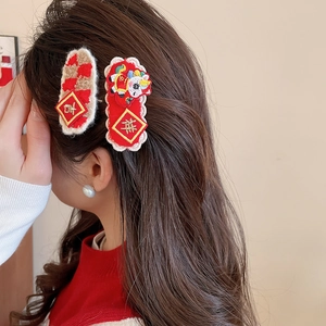 Detail showing two red New Year hair clips with intricate embroidery worn by a model