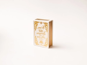 Close-up of white book-shaped ceramic vase with gold text and fairy tale patterns