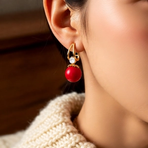 Detailed close-up of a red resin bead earring with zircon accents on a golden ear hook
