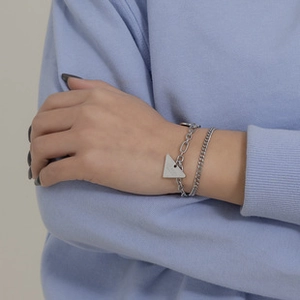 Detail of a silver double-layer link bracelet with a signature triangle charm on wrist