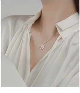 Detail of a crescent moon pearl necklace in 925 silver worn on a silk white shirt