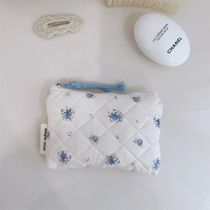Détail d'une pochette en coton matelassé à fleurs avec tirette de fermeture bleue