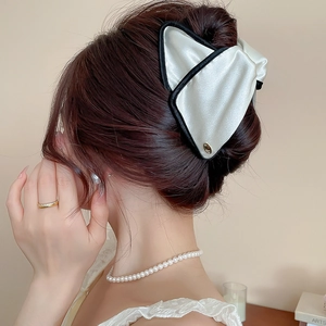 Detail view of a large white silk bow hair claw clip with black edges on a half-up hairstyle
