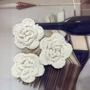 Detailed view of three handmade off-white crochet yarn flowers for garment accessories
