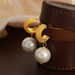 Elegant gold textured hoop earrings with large white pearls shown in a close-up profile