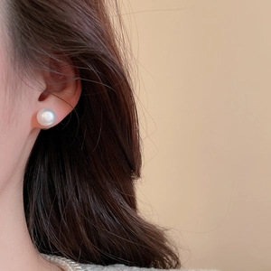 Close-up of a large white round pearl earring with satin luster on a model ear