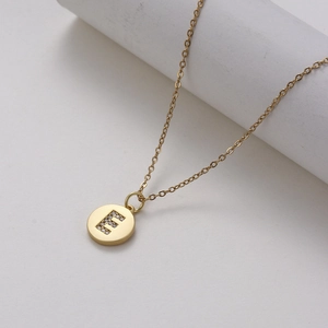 Macro view of a gold-plated necklace with a micro-paved zircon letter E pendant on a cylinder