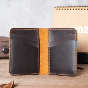 Handmade vintage leather card holder with slim bifold design on a rustic wooden desk