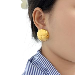 Golden earrings with woven grid texture on female model shown from a side profile view