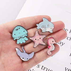Handheld set of five ocean theme enamel pins featuring shark jellyfish and starfish