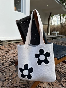 Close-up of beige knitted tote bag with black flower patterns hanging on wooden chair