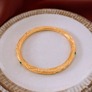 Détail d'un bracelet jonc plaqué or 18k avec pierre verte sur plateau céramique