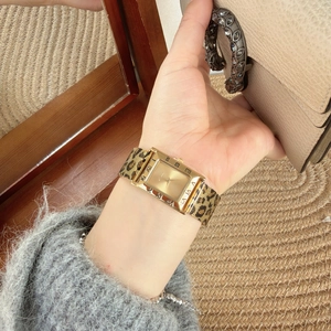 Detail of a gold rectangular quartz watch with leopard print metal strap on woman's wrist