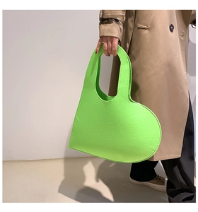Close-up of vibrant neon green felt heart-shaped handbag held by a fashion model
