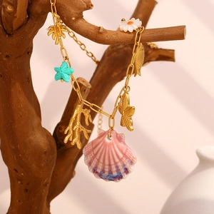 Bracelet doré océan avec coquillage rose et corail suspendu à une branche en bois