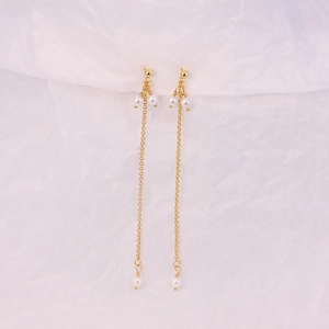 Detail of elegant gold chain tassel earrings with white pearls on a soft white fabric