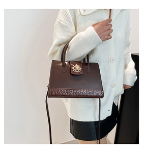 Detail of dark brown shoulder bag with crocodile texture and gold floral clasp on model