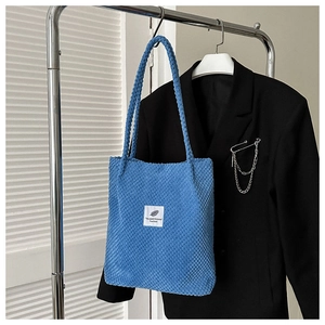 Detail of blue textured fleece tote bag with white decorative patch and chain accent