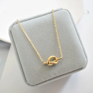 Close-up of golden knot pendant necklace on a premium gray velvet jewelry box